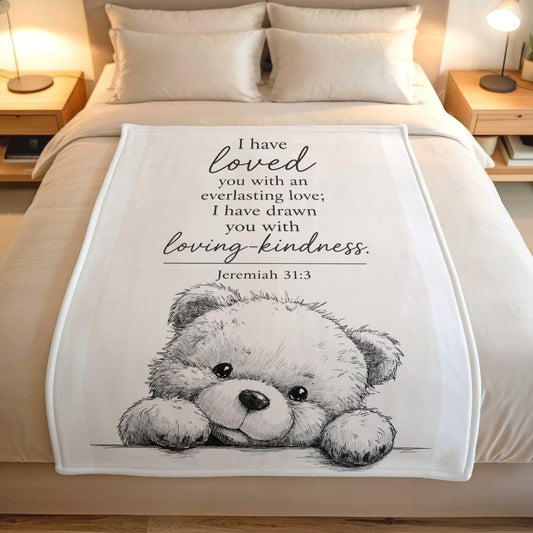 Lightweight fleece blanket with teddy bear and Jeremiah 31 verse on a bed