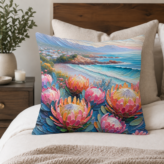 Coastal Protea 45 × 45 cm cotton scatter cushion styled on a neutral bed, featuring colourful proteas, blue mountains and a seaside scene.