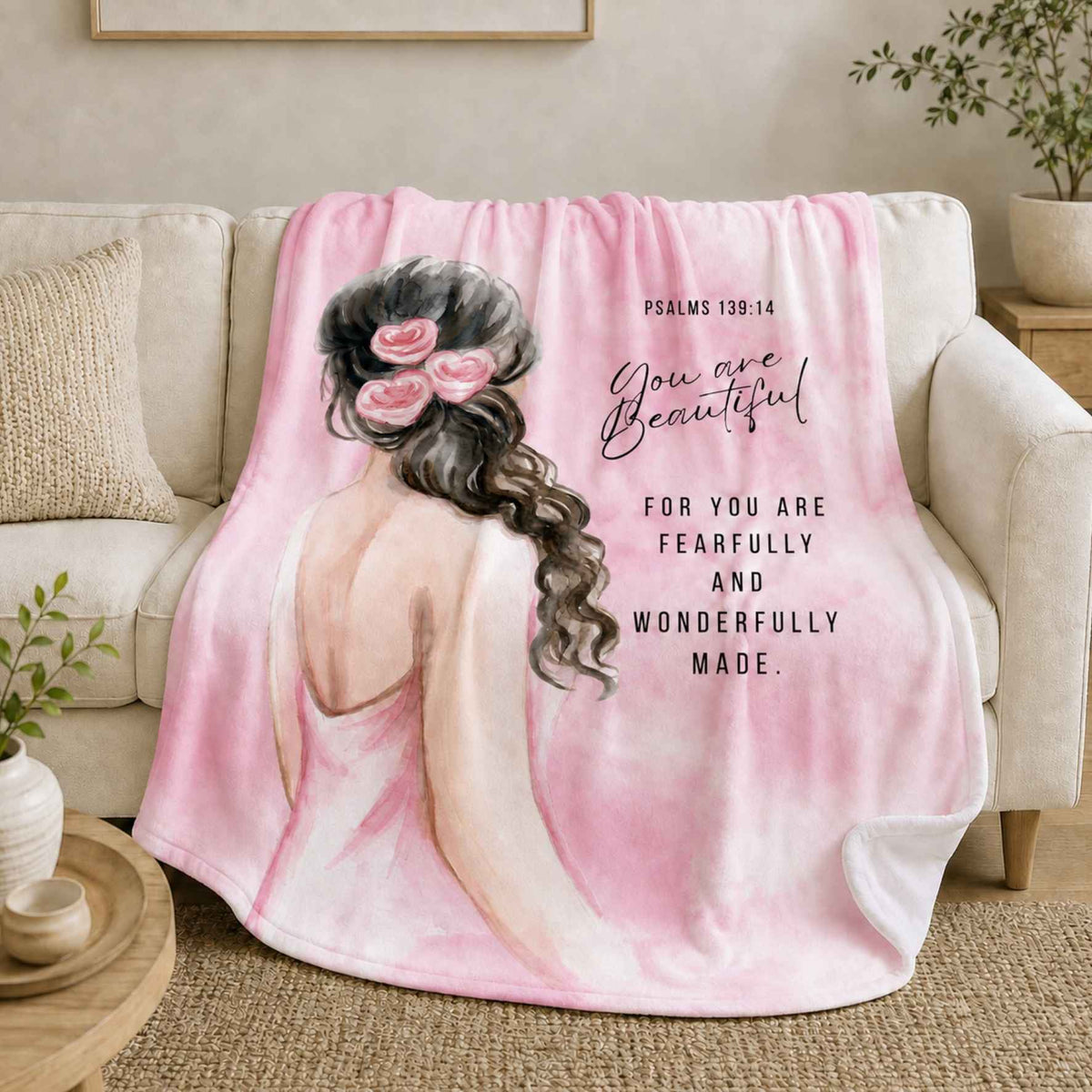 Pink Psalm 139:14 You Are Beautiful lightweight fleece blanket with a watercolour girl, draped over a cream sofa in a neutral living room.